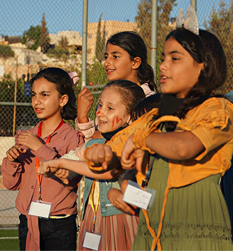 A group of five smiling young girls outdoors, looking towards the right.